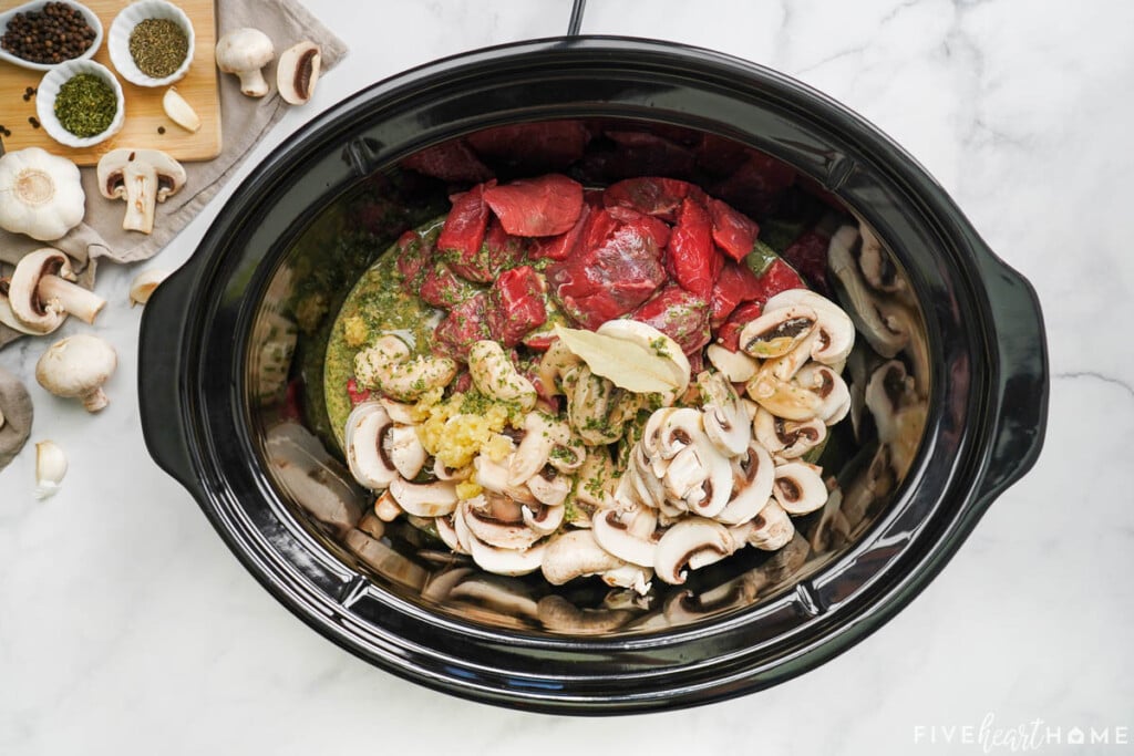 Slow Cooker with beef, mushrooms, garlic, and sauce ingredients.