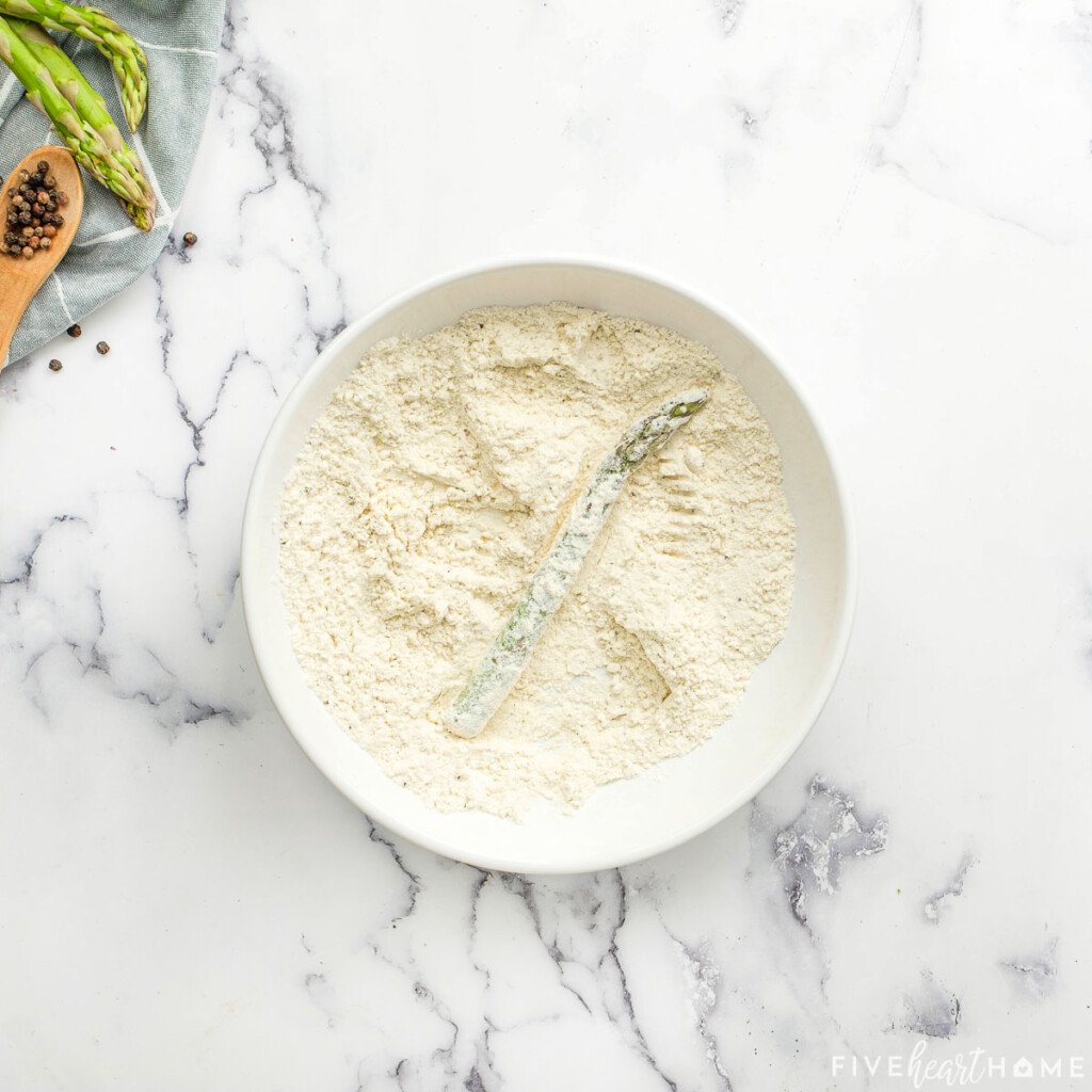 Dipping spear in flour for breaded asparagus recipe.