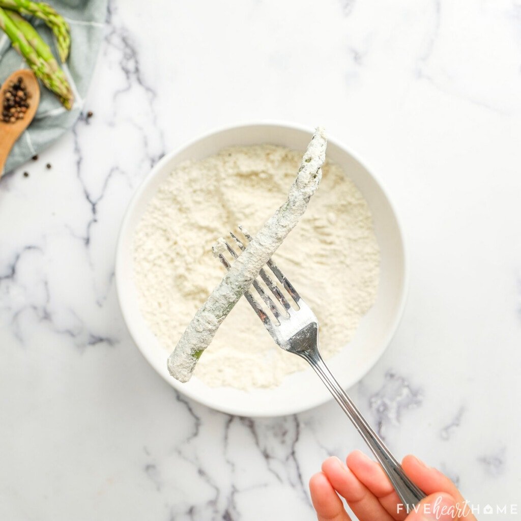 Lifting breaded asparagus spear out of flour with fork.