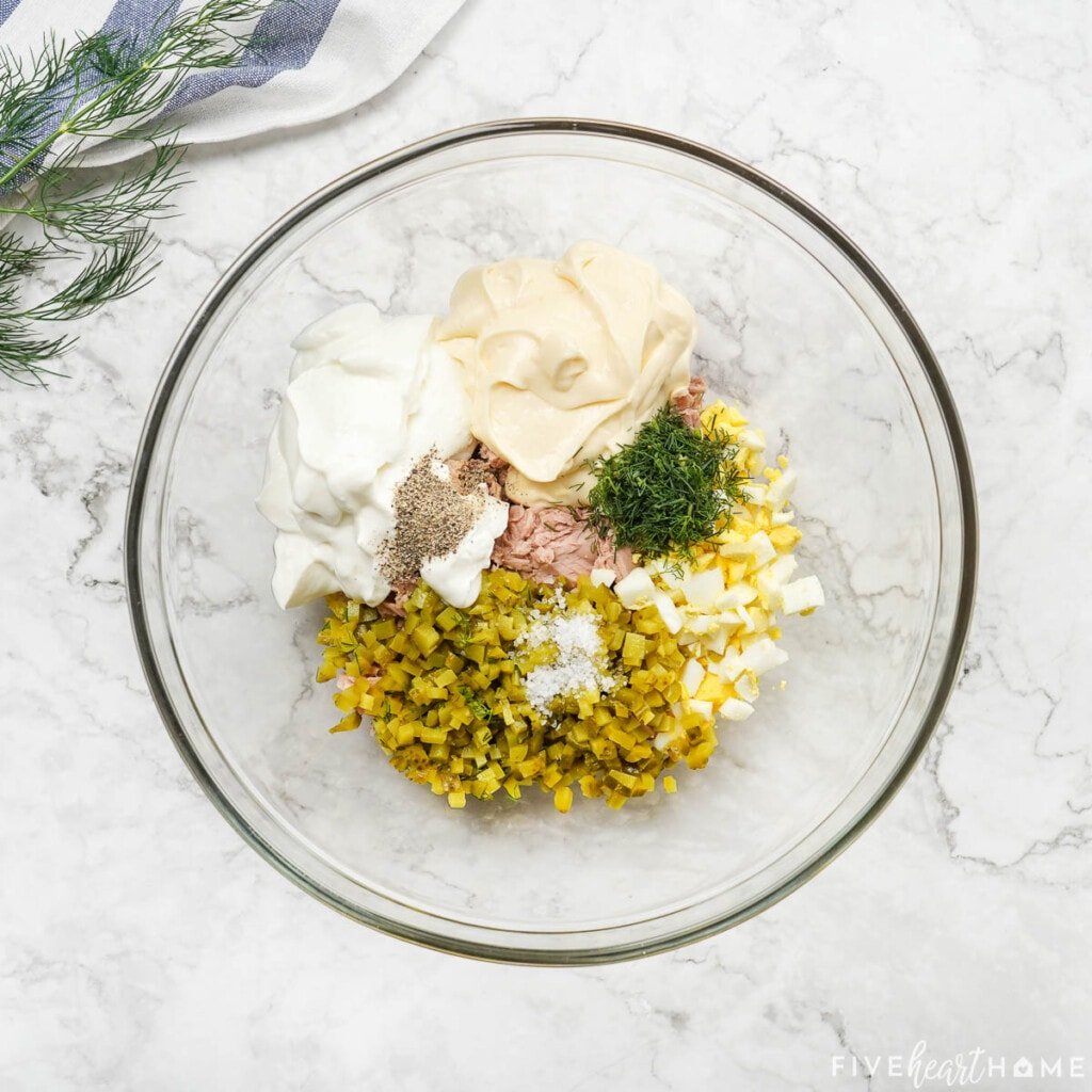 Tuna, mayonnaise, Greek yogurt, egg, pickles, seasonings, and fresh dill in bowl.