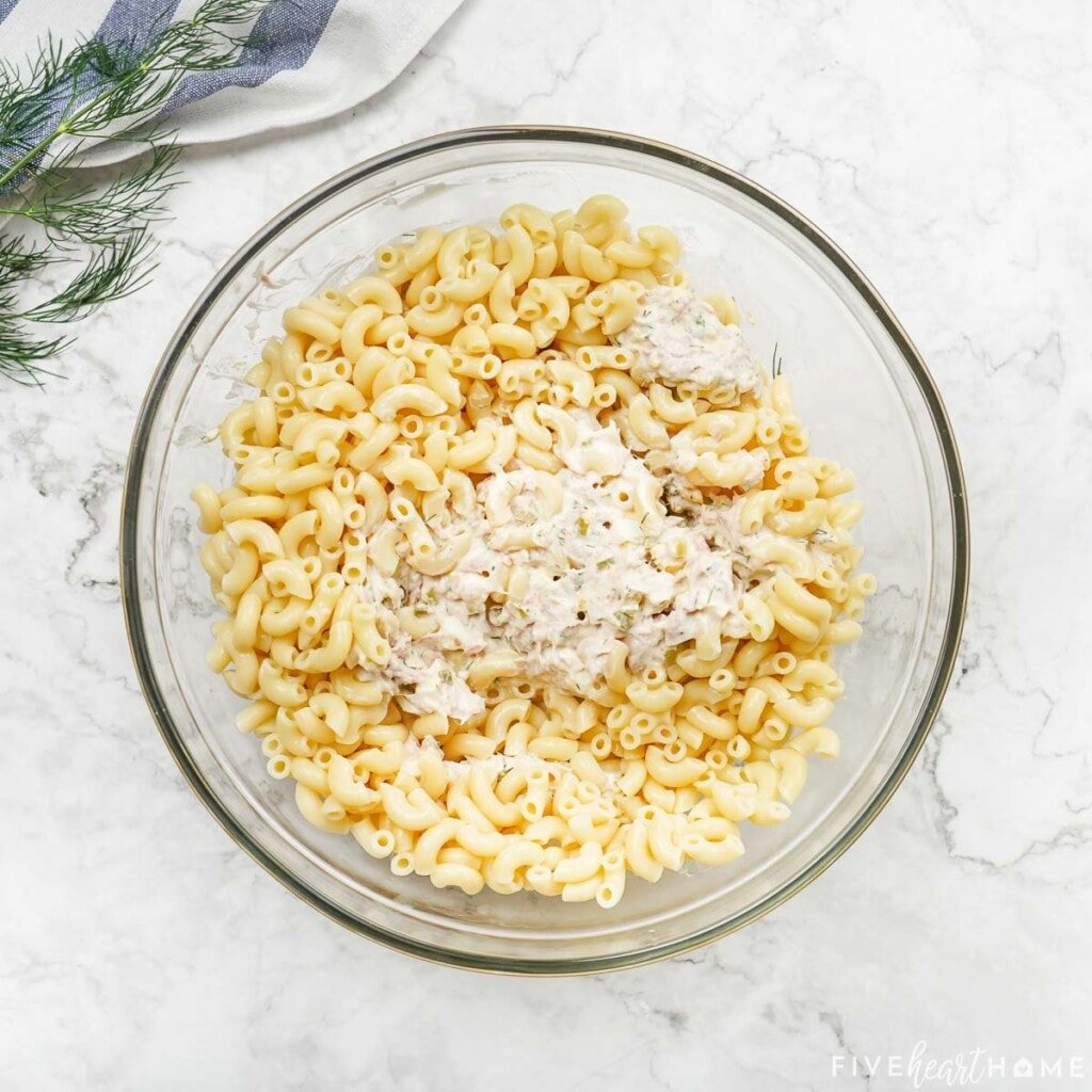 Stirring dressing into macaroni for pasta tuna salad recipe.