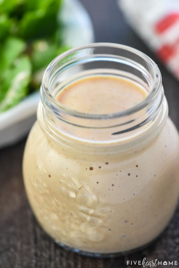 Homemade Thousand Island Dressing in glass jar with salad in background.