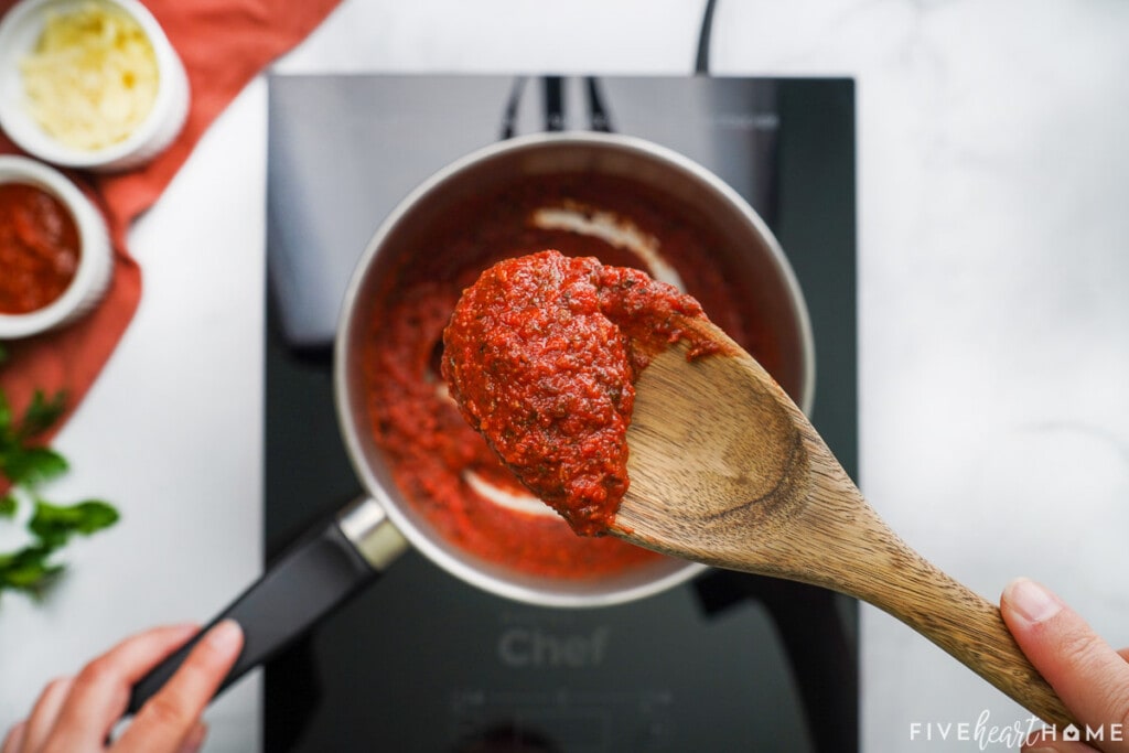 Pizza sauce on wooden spoon over pot.