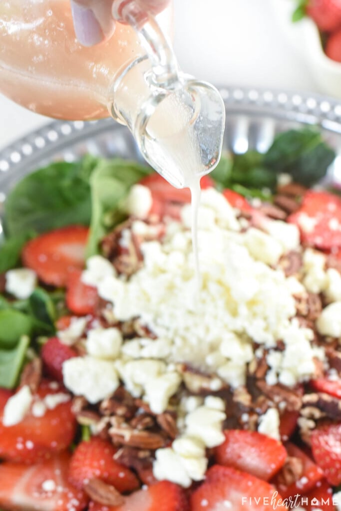 Pouring Blush Wine Vinaigrette over Spinach Salad with Strawberries.