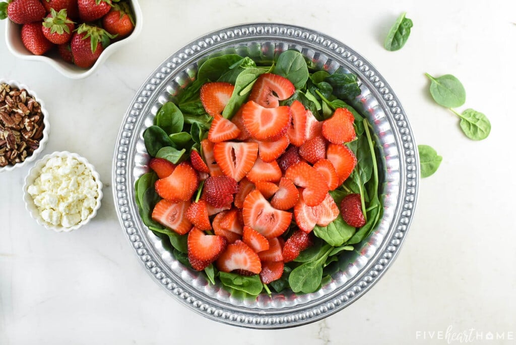 Sliced strawberries on top of baby spinach.