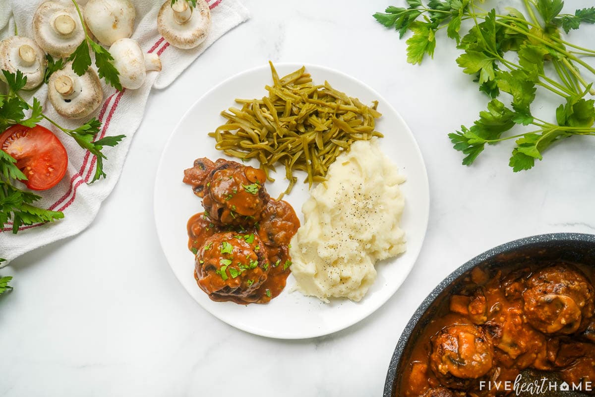 Aerial view of hamburger steak recipe on plate with mashed potatoes and green beans.