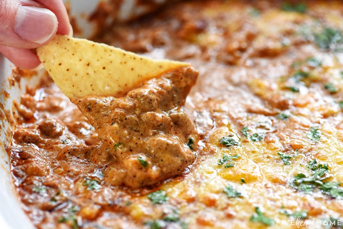 Scooping up Beef Enchilada Dip onto tortilla chip.