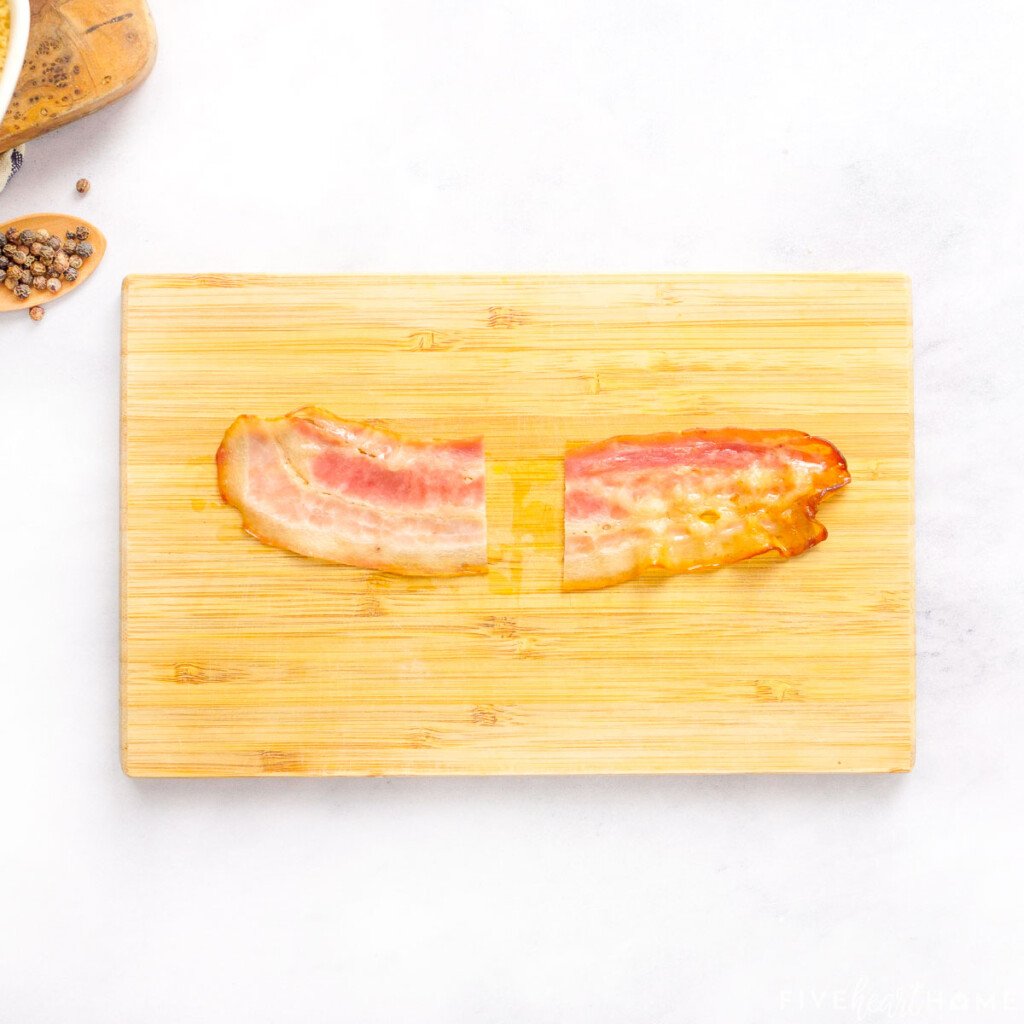 Cooked bacon cut in half on cutting board.