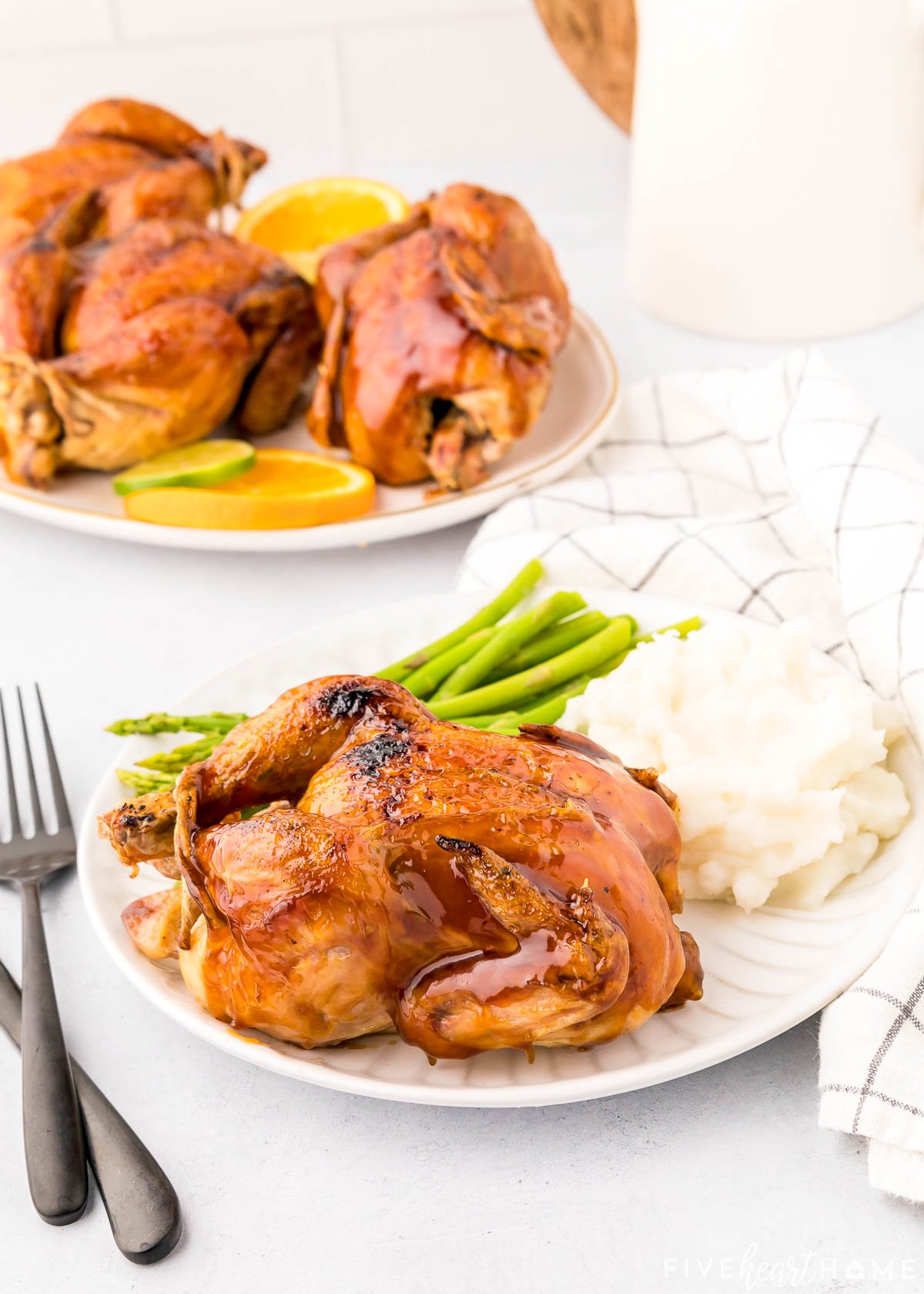 Cornish hen on plate with sides and additional Cornish hens on platter in background.