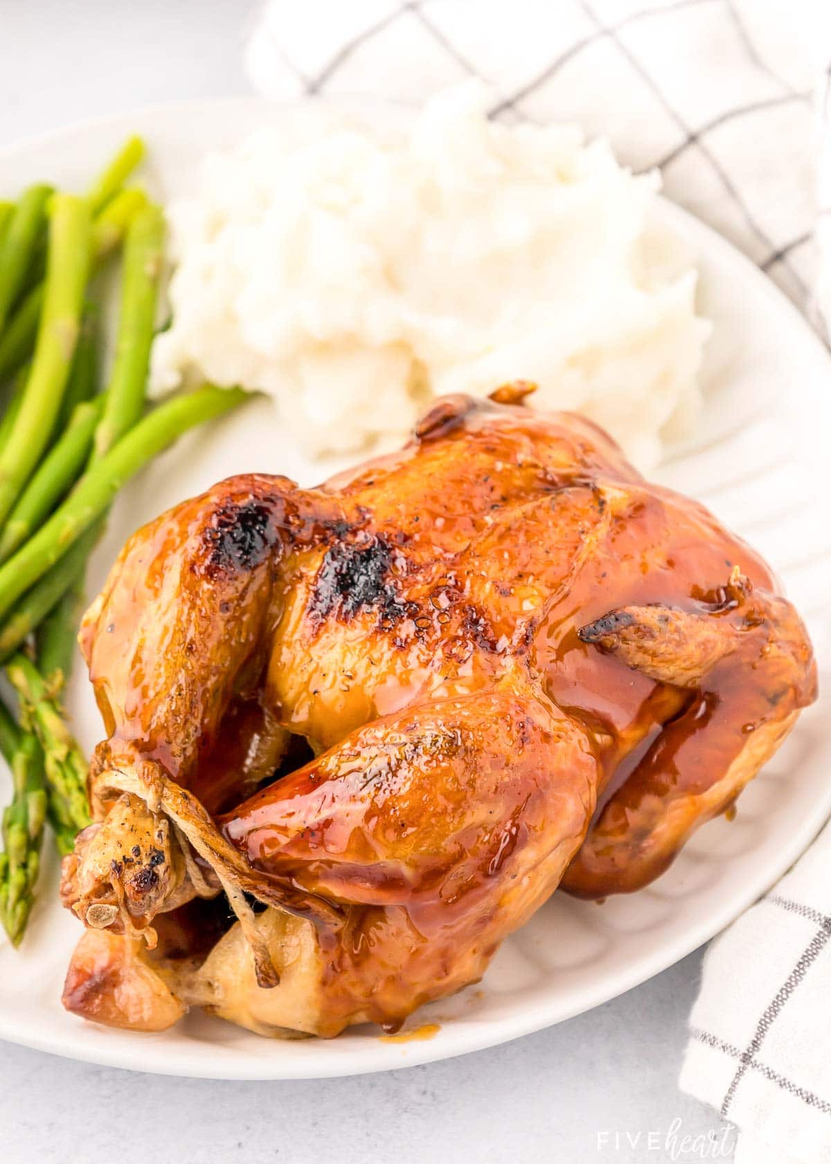 Cornish hen with mashed potatoes and asparagus on plate.