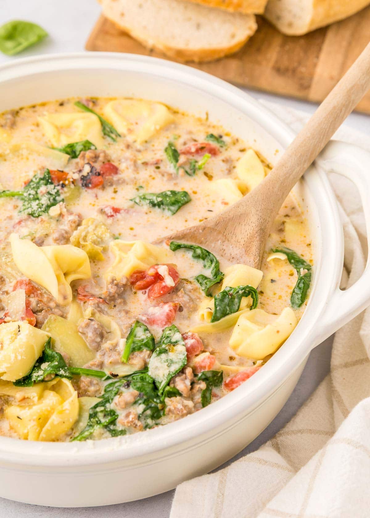 Sausage Tortellini Soup recipe with wooden spoon.
