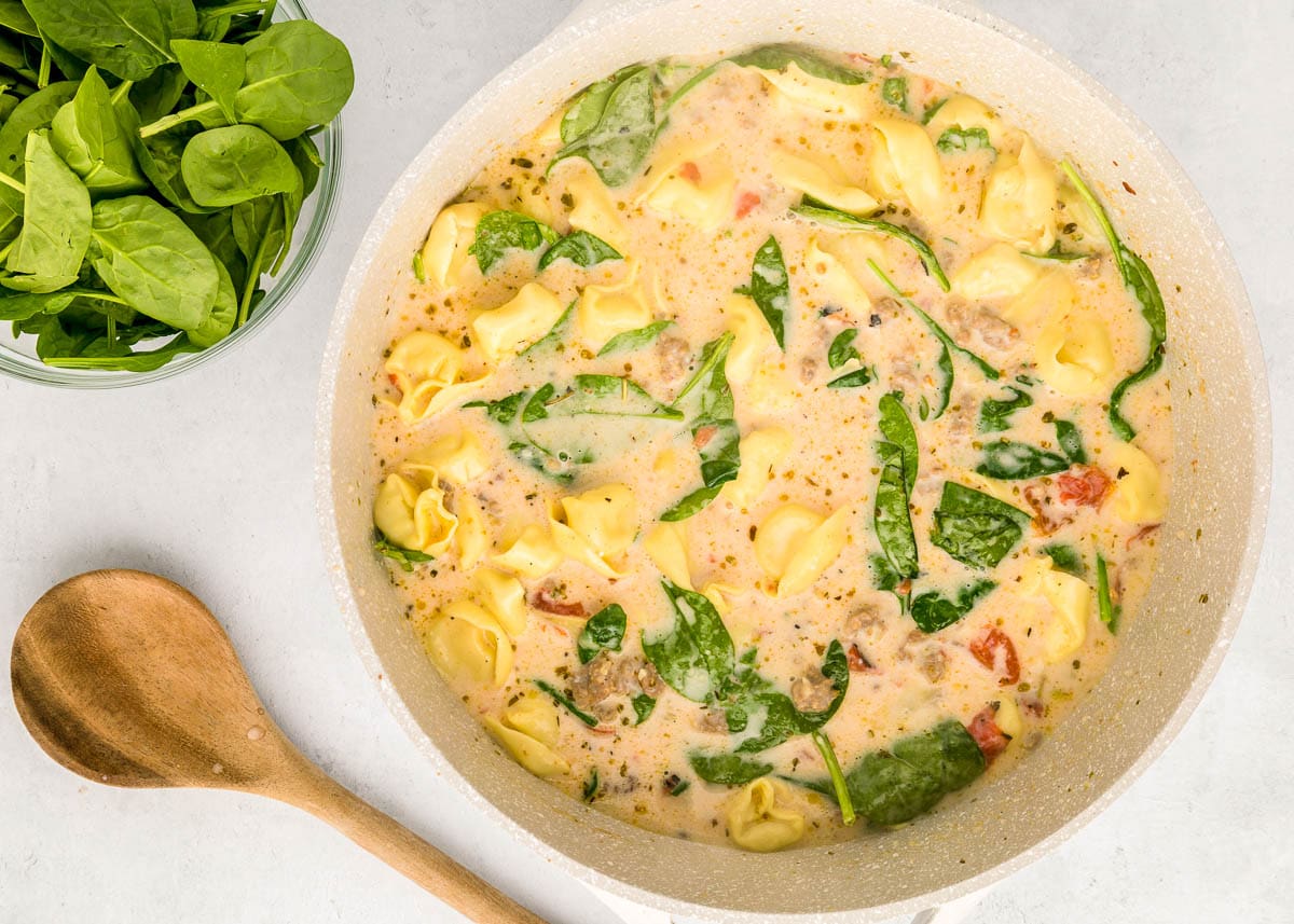 Adding half-and-half and spinach to creamy Sausage Tortellini Soup.