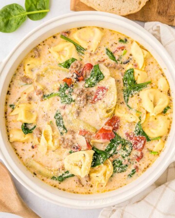 Sausage Tortellini Soup in white pot with wooden spoon.