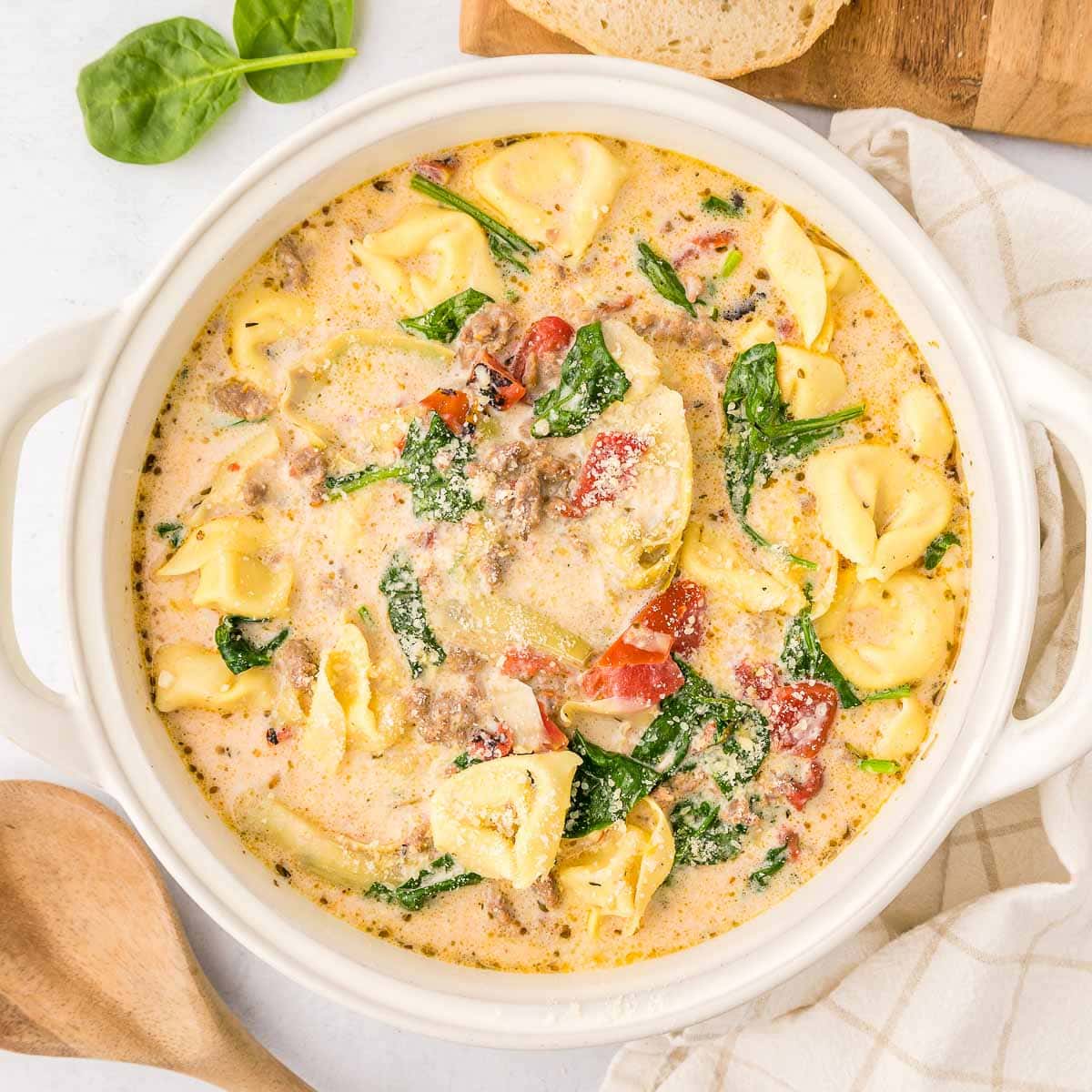 Sausage Tortellini Soup in white pot with wooden spoon.