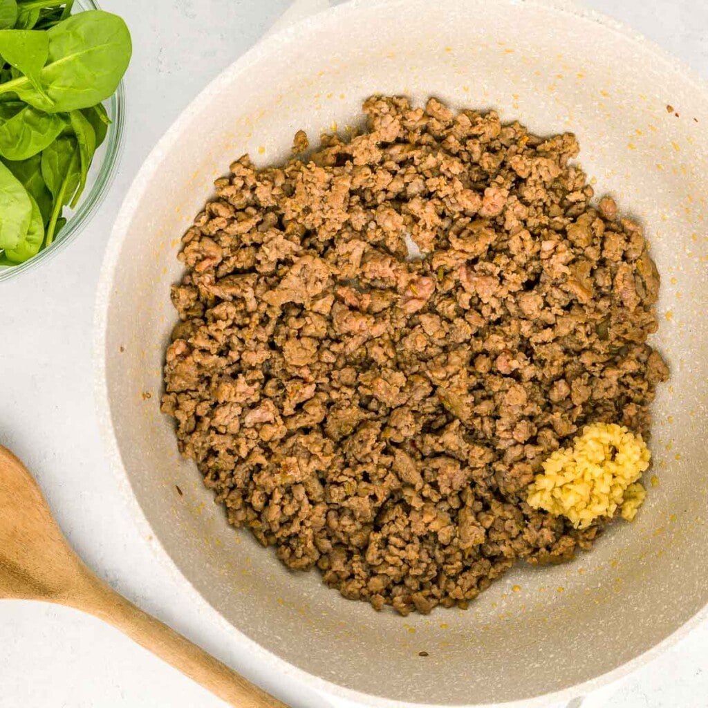 Adding garlic to Italian sausage in pot.