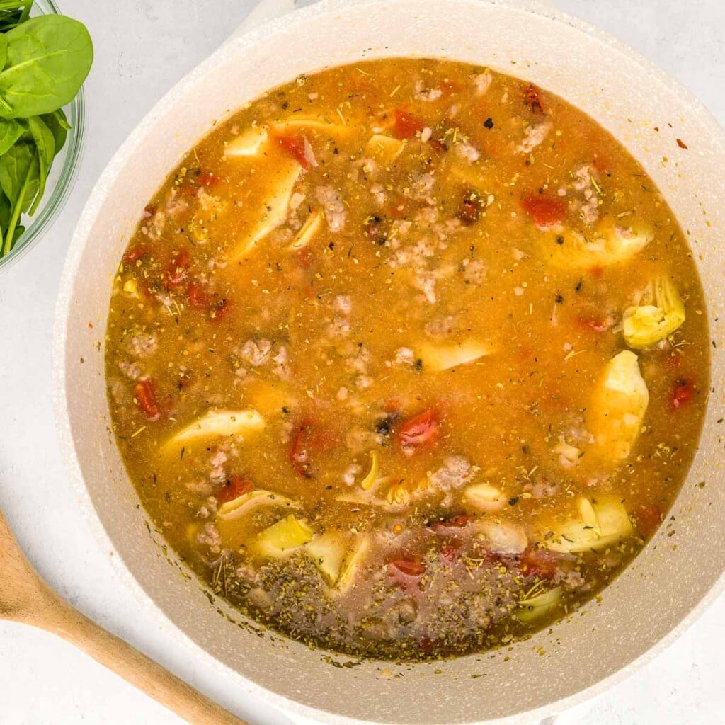 Adding remaining ingredients for Sausage Tortellini Soup recipe.