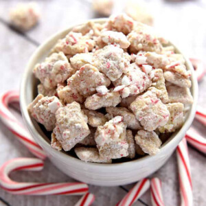 Christmas Puppy Chow (or Christmas Muddy Buddies) in a bowl surrounded by candy canes.