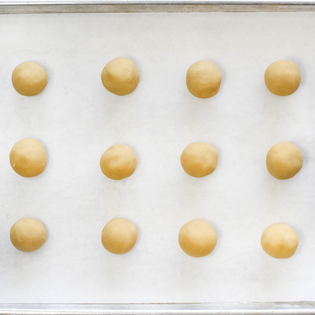 Rolled balls of cookie dough on baking sheet for Jam Thumbprint Cookies.