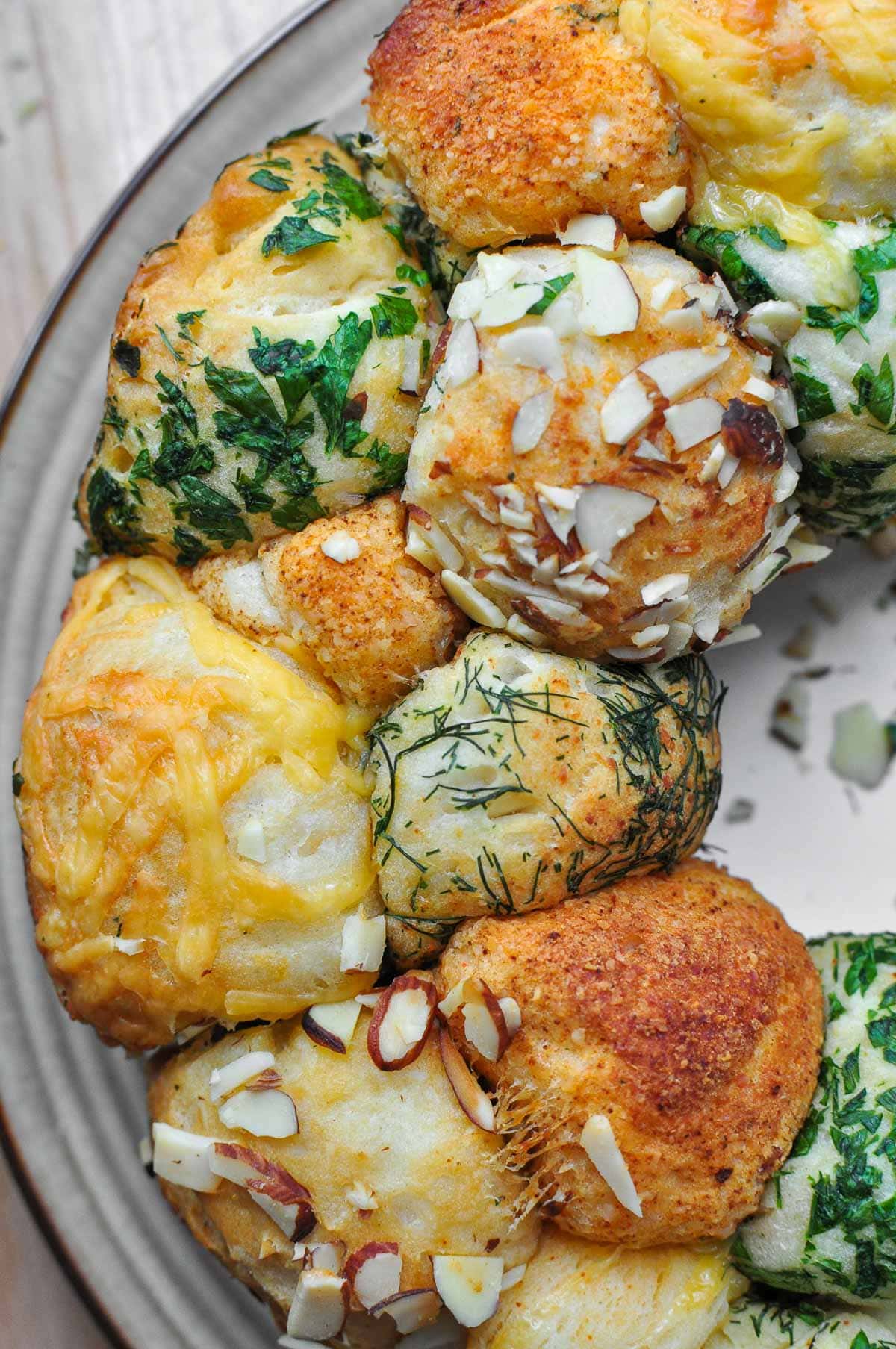 Close-up of monkey bread coated with fresh herbs, slivered almonds, cheddar, and Parmesan.