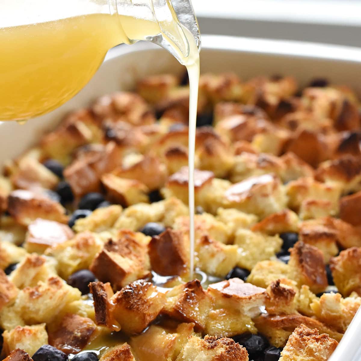 Overnight Lemon Blueberry French Toast Casserole in dish with lemon syrup being poured.