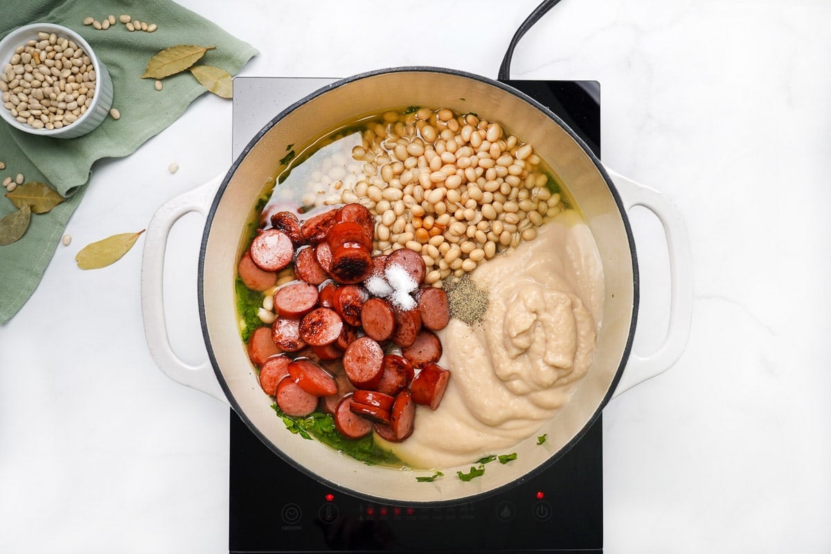 Adding sausage and remaining ingredients to white bean and kale soup.