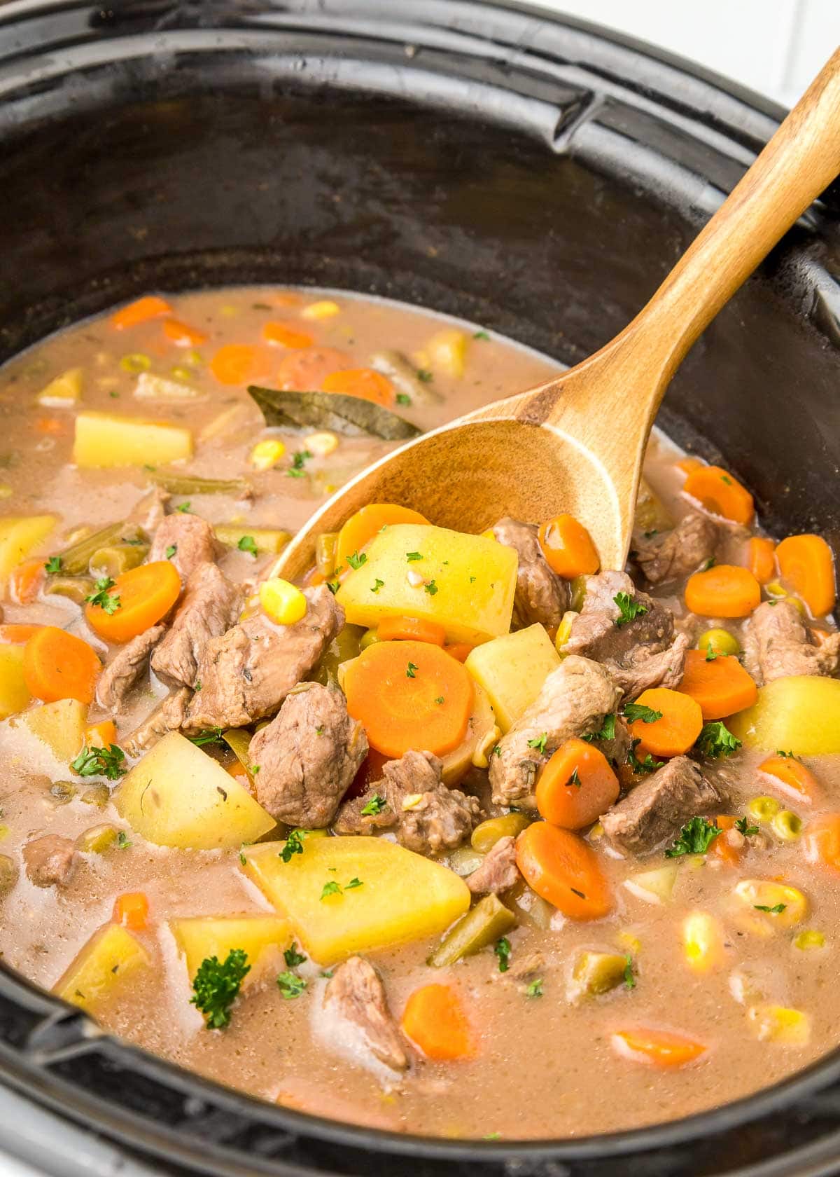 Wooden spoon stirring recipe for beef stew in crock pot.