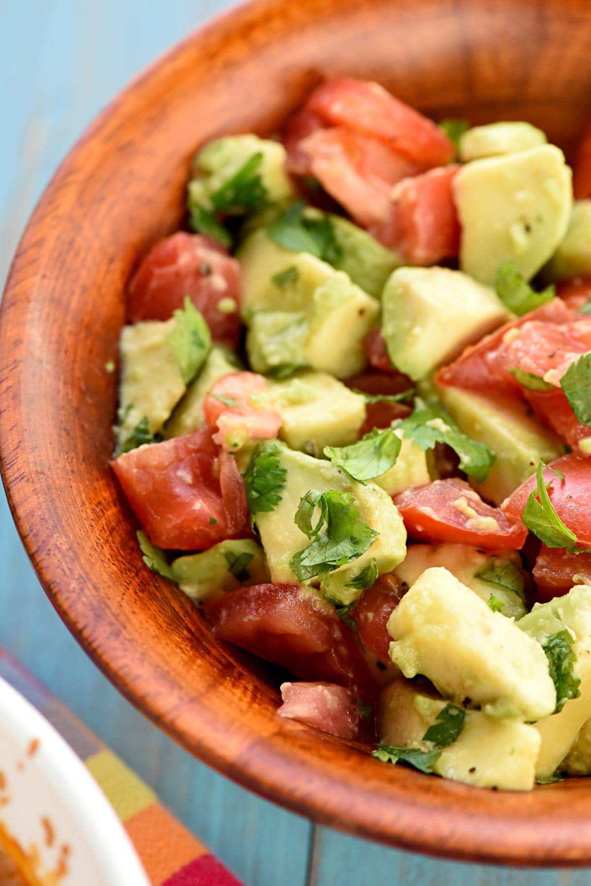 Avocado tomato salad in wooden bowl.