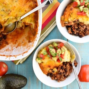 Taco Bake in casserole dish and bowls topped with avocado tomato salad.