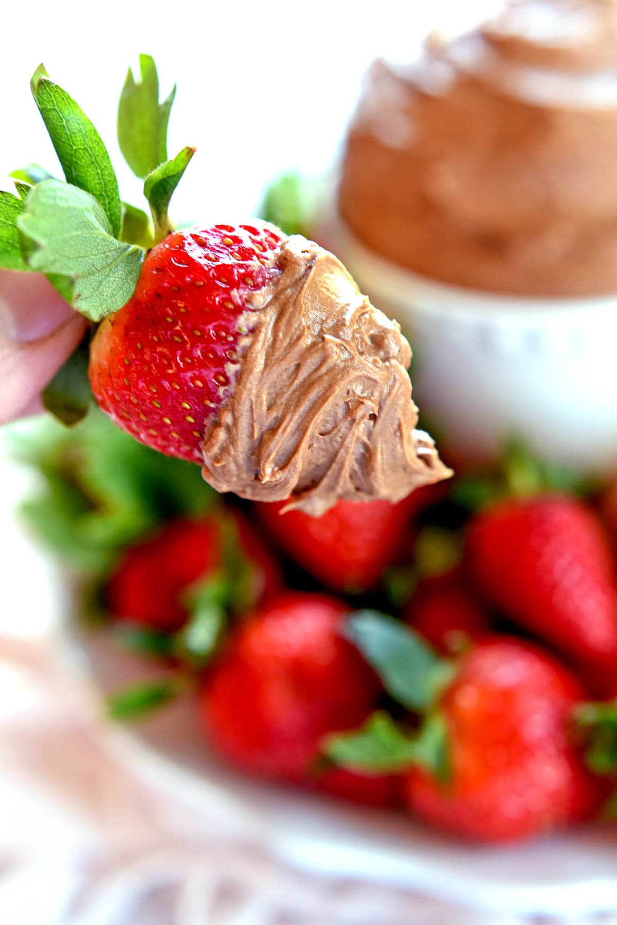 Chocolate Fruit Dip on strawberry with bowl and berries in background.