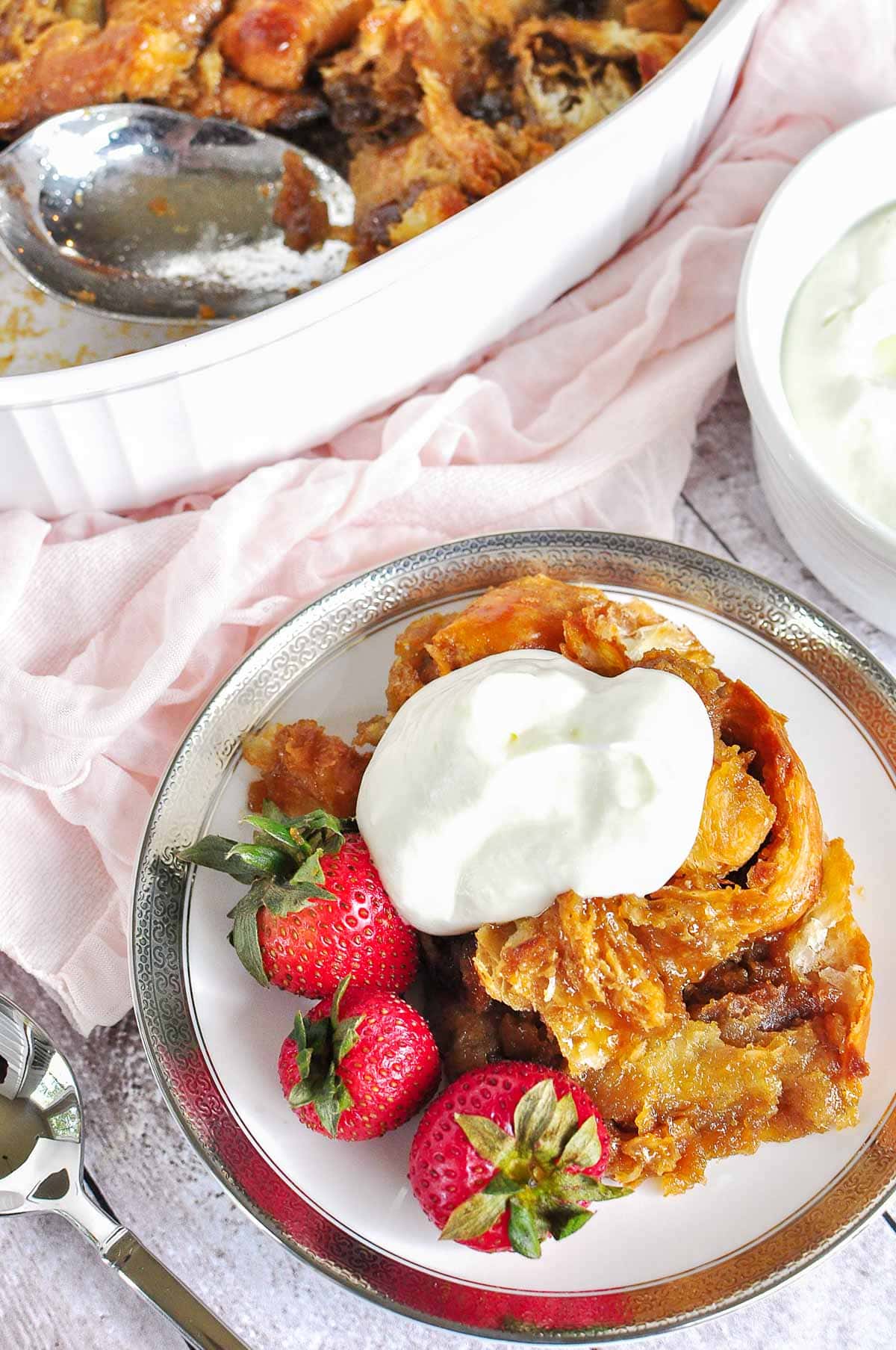 Croissant Bread Pudding in dish and on plate with whipped cream and berries.