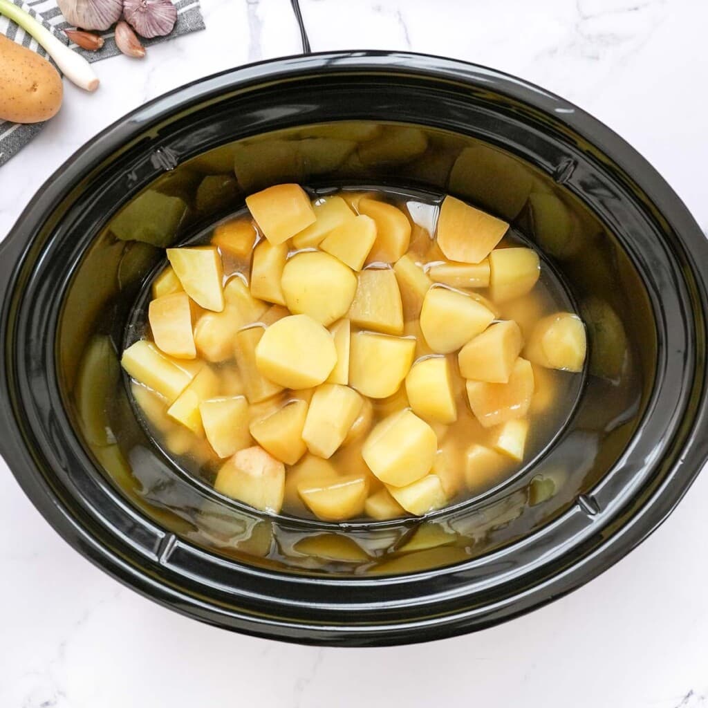 Potatoes and broth in slow cooker for loaded baked potato soup crock pot.