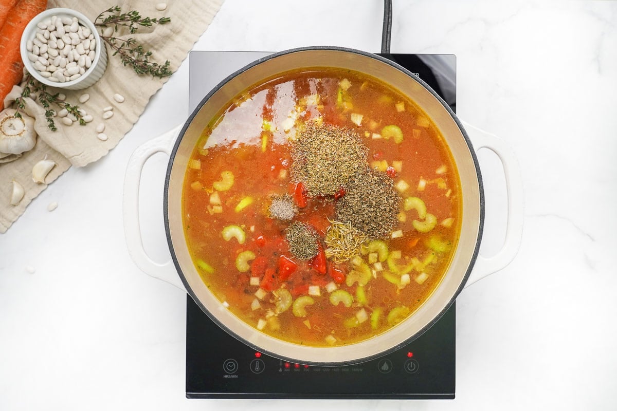 Adding liquid, tomatoes, seasonings, and pasta to Minestrone Soup recipe.