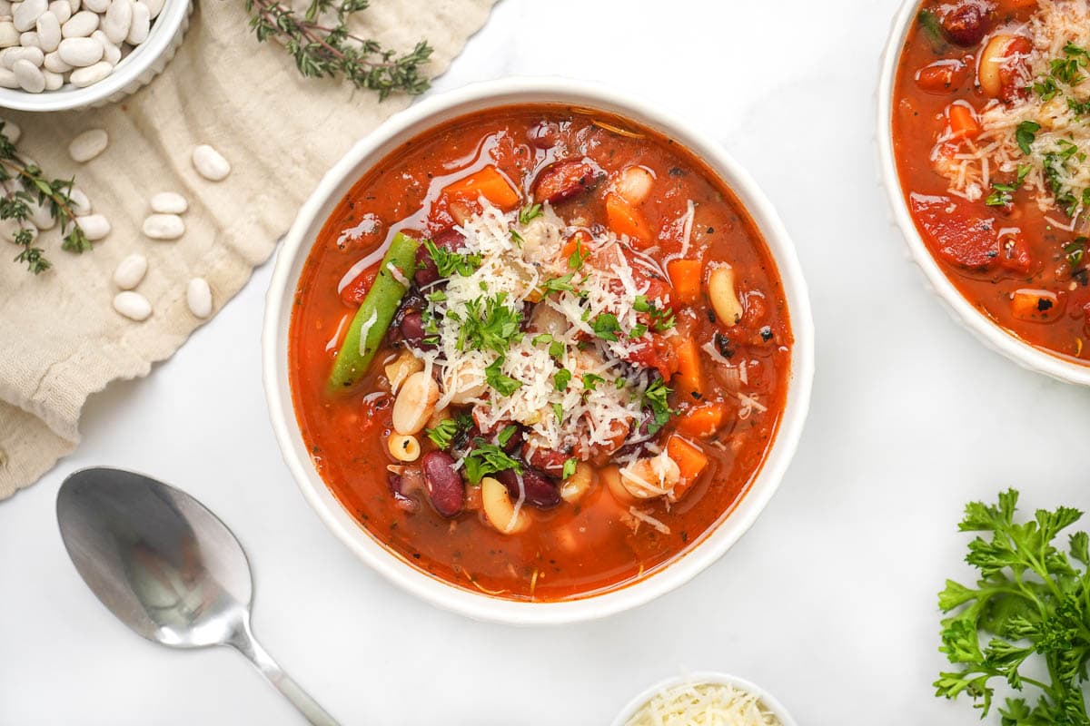 Aerial view of Minestrone Soup recipe in two bowls with spoon on table.