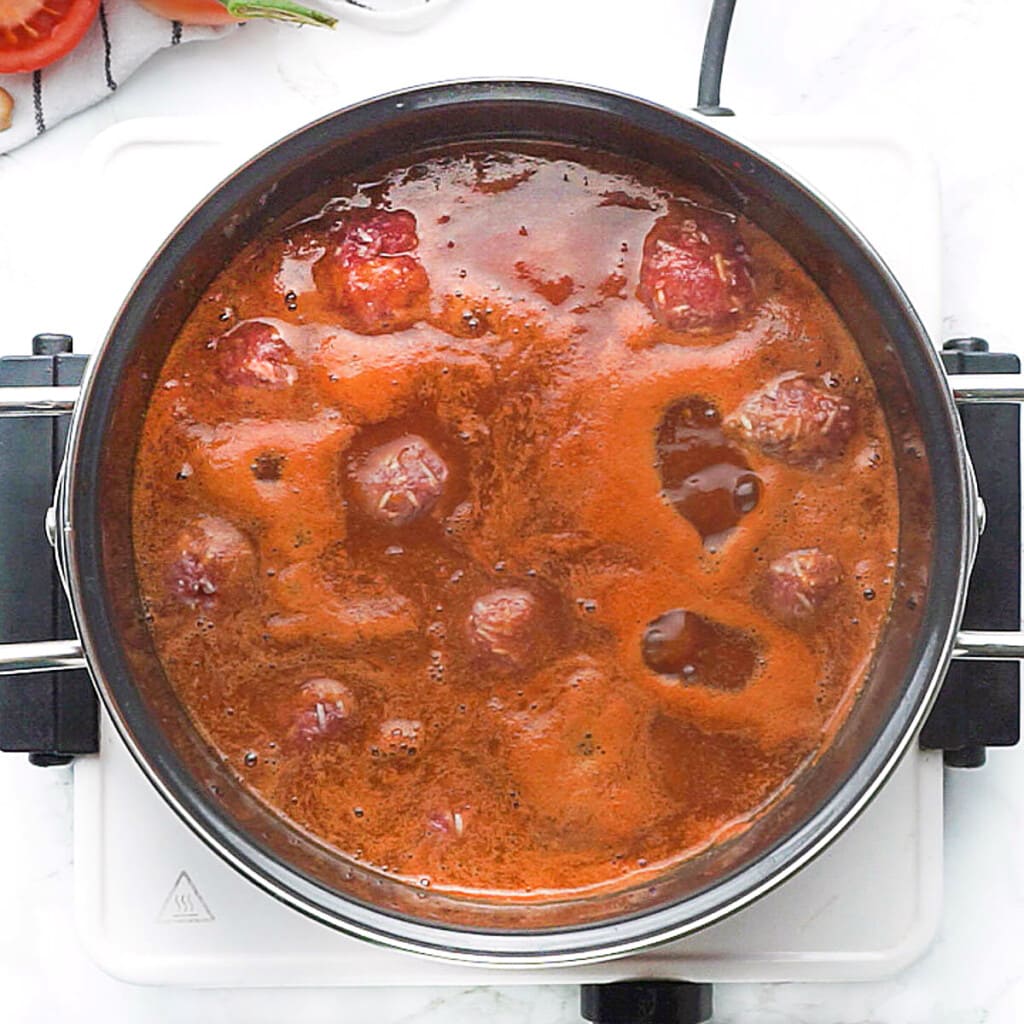 Porcupine Meatballs dropped into pot of tomato sauce.