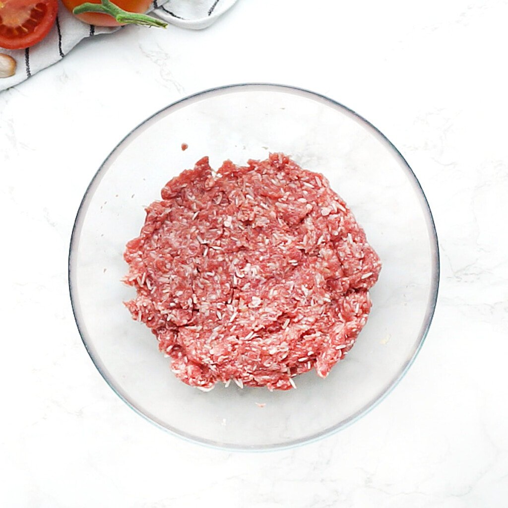 Meatball mixture combined in glass bowl.