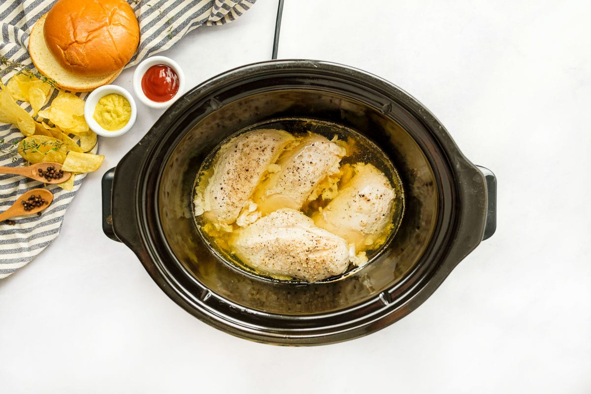 Slow cooker of cooked chicken breasts.