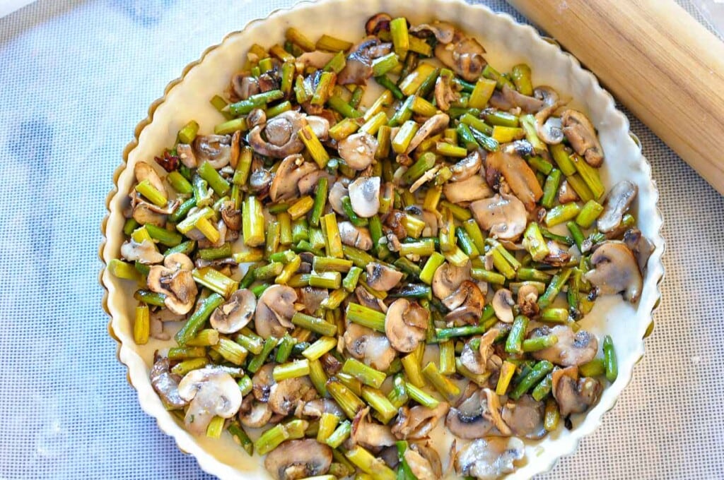 Sauteed asparagus and mushrooms filling pie crust in pan.