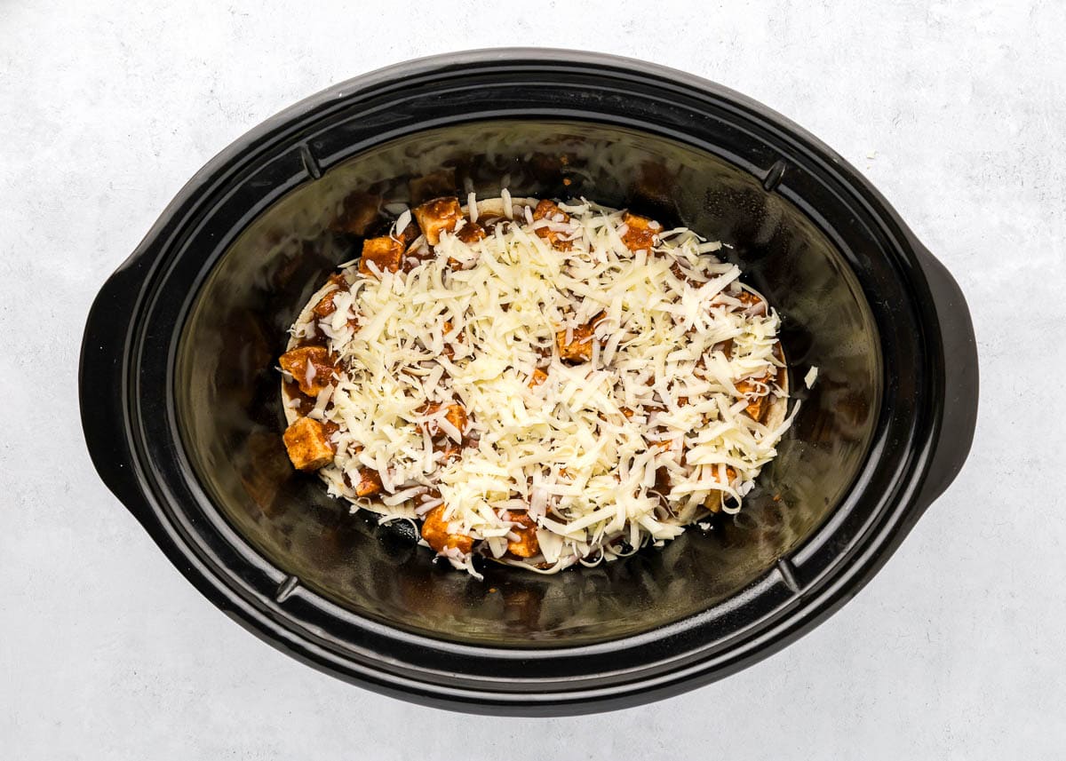 Adding cheese to slow cooker chicken enchilada casserole.