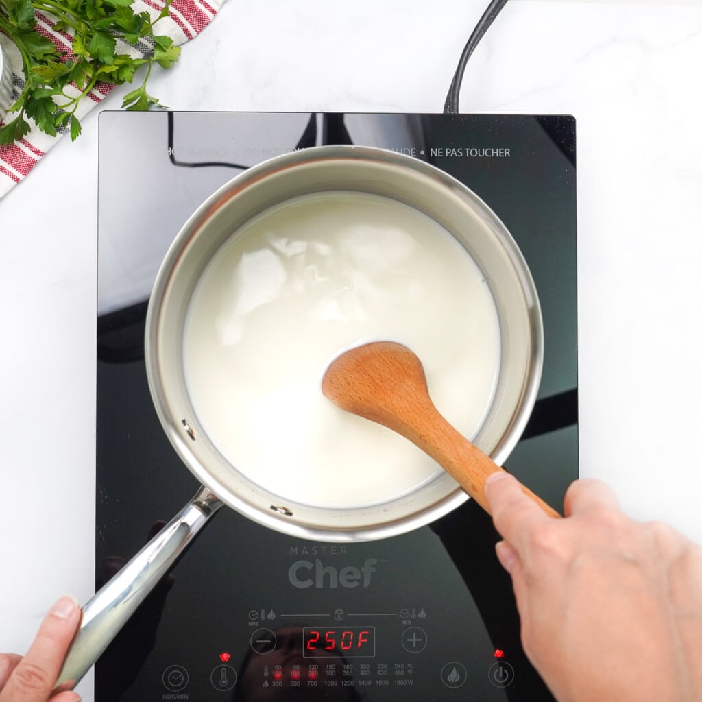 Stirring grits into milk on stove with wooden spoon.
