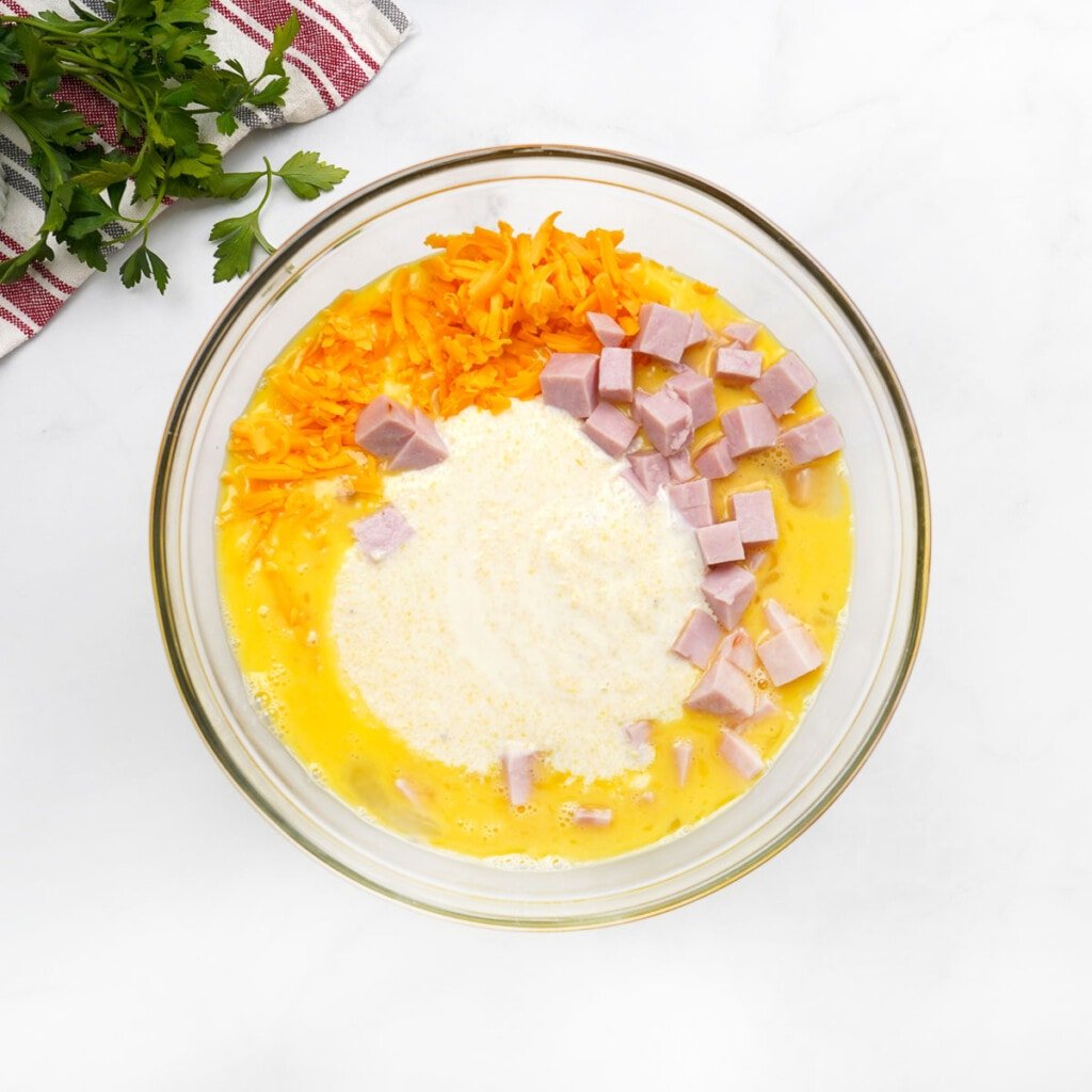 Grits, cheese, and ham added to eggs for Grits Casserole recipe.