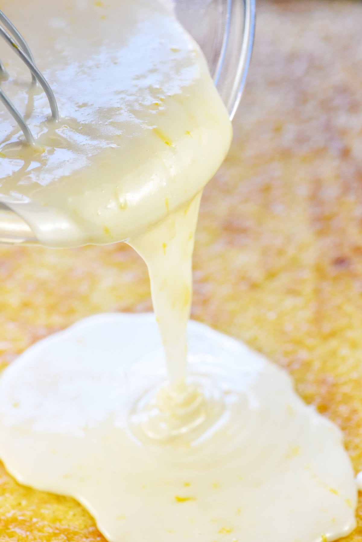 Lemon glaze being poured over lemon sheet cake.