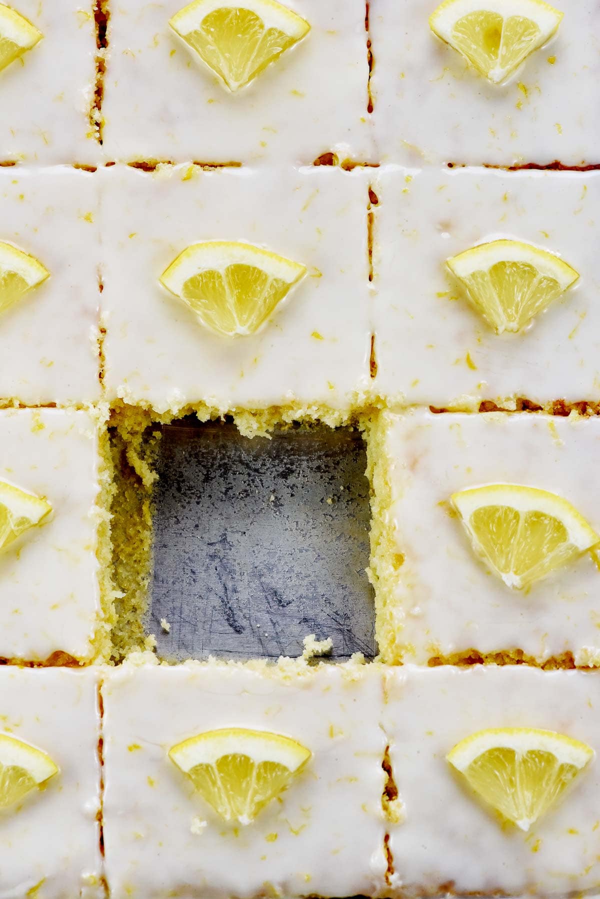 Aerial view of Lemon Sheet Cake with lemon glaze for cake, sliced in pan with missing piece.