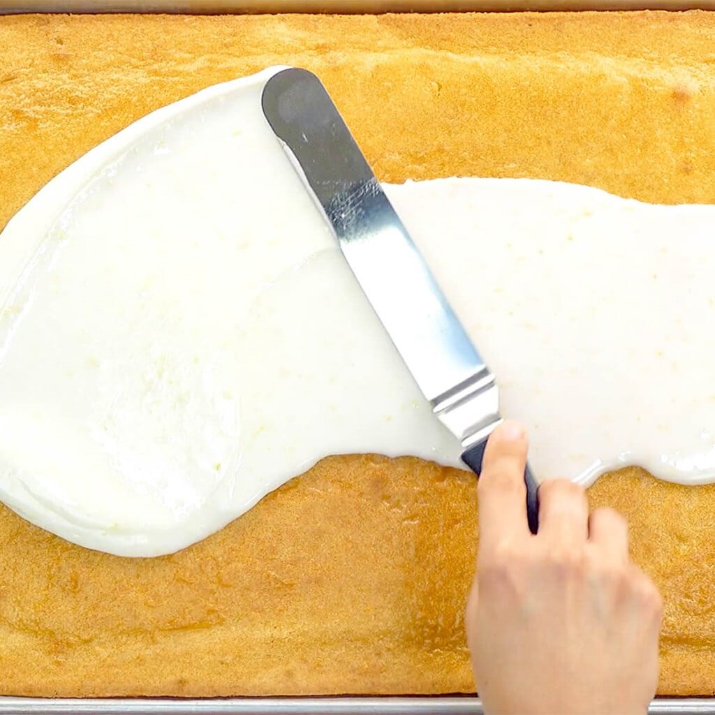 Spreading lemon glaze over easy Lemon Sheet Cake.