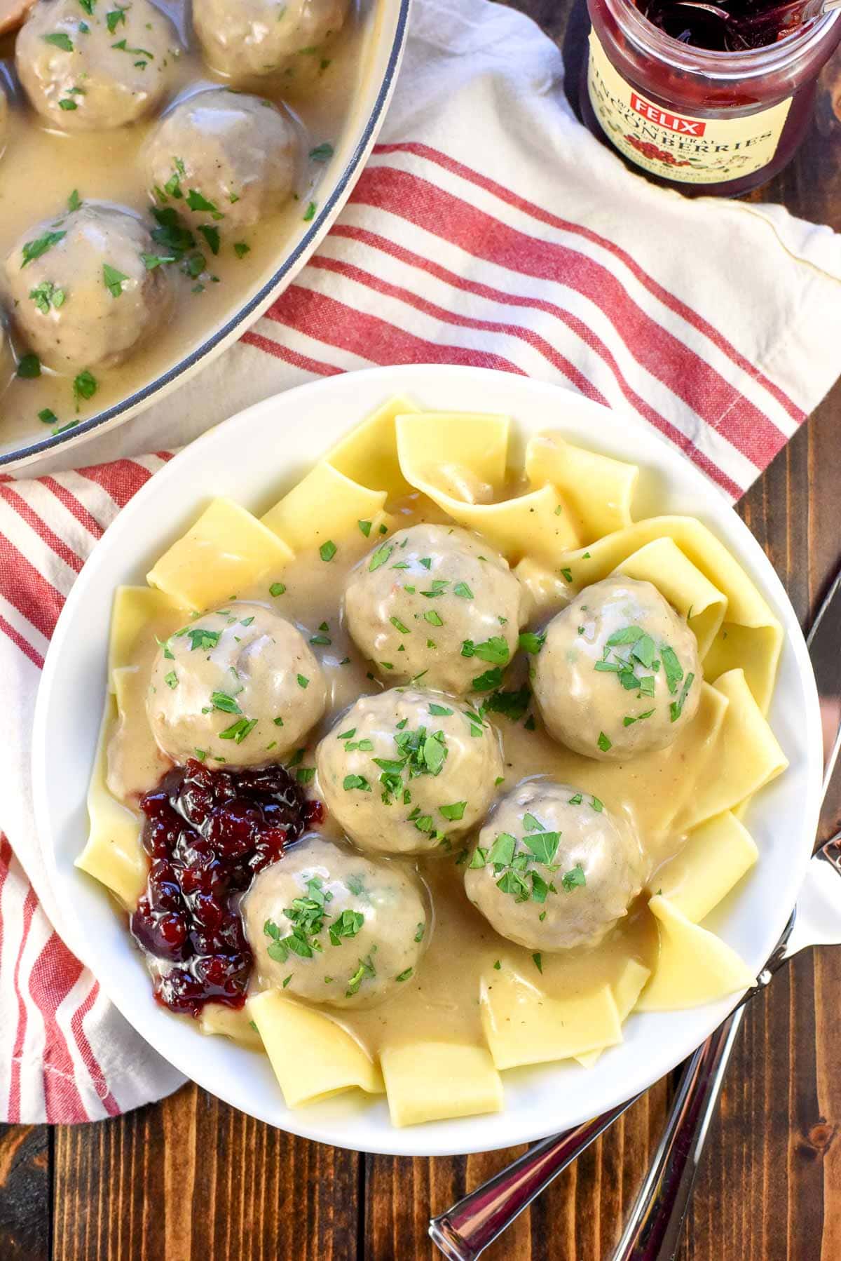 Aerial view of Swedish Meatball recipe over noodles with sauce, parsley, and lingonberry jam.