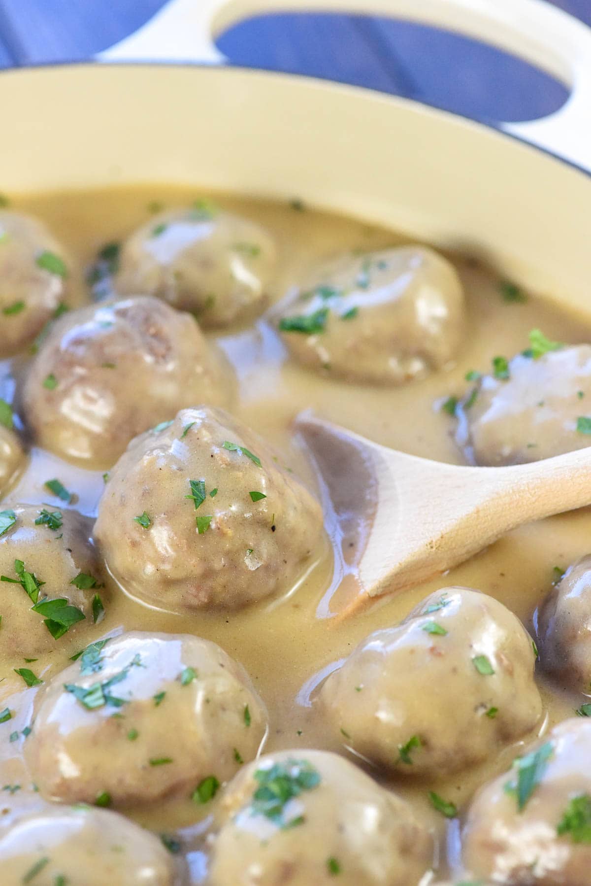Wooden spoon scooping Swedish Meatballs out of sauce.