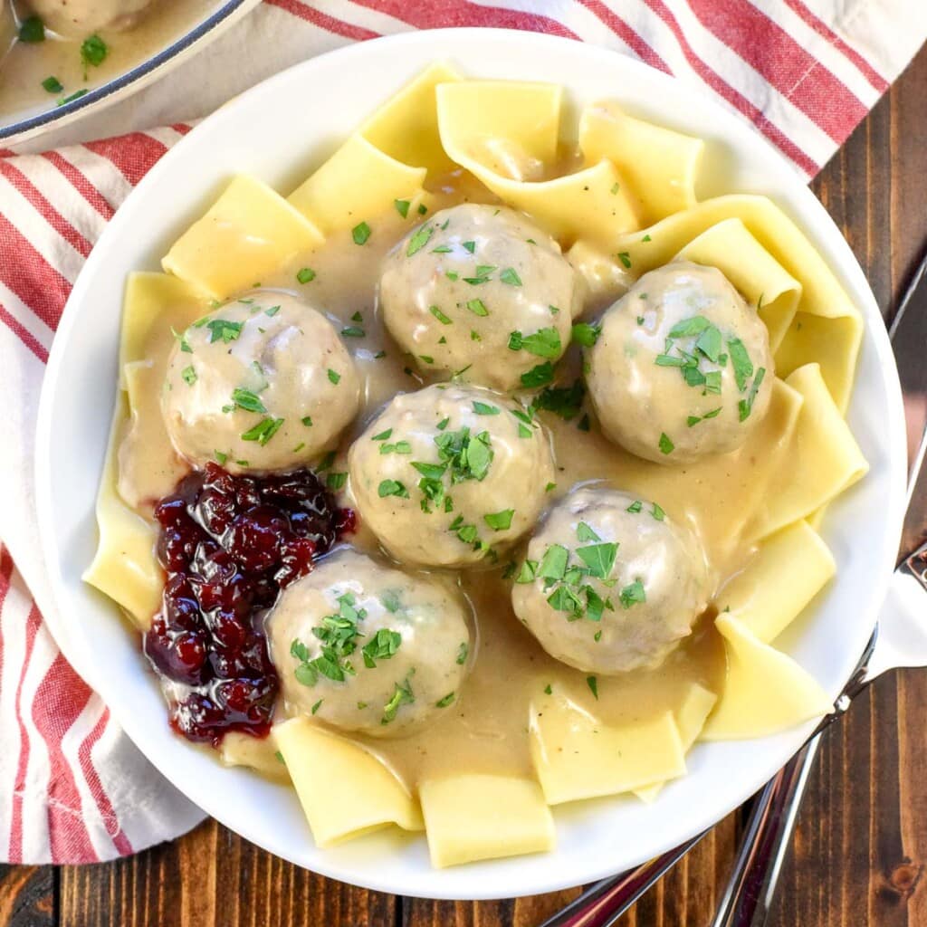 Swedish Meatballs on plate with noodles, sauce, lingonberries, and parsley.