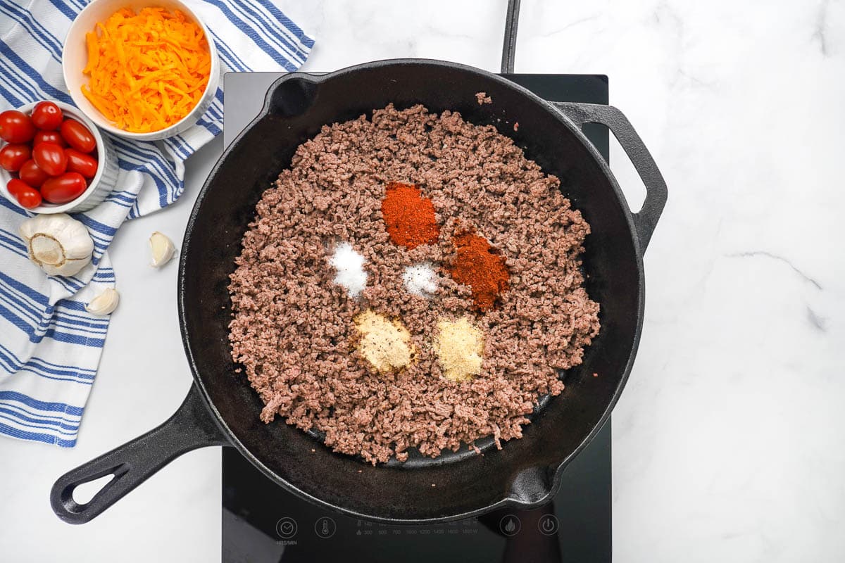 Adding spices to cooked ground beef in skillet.