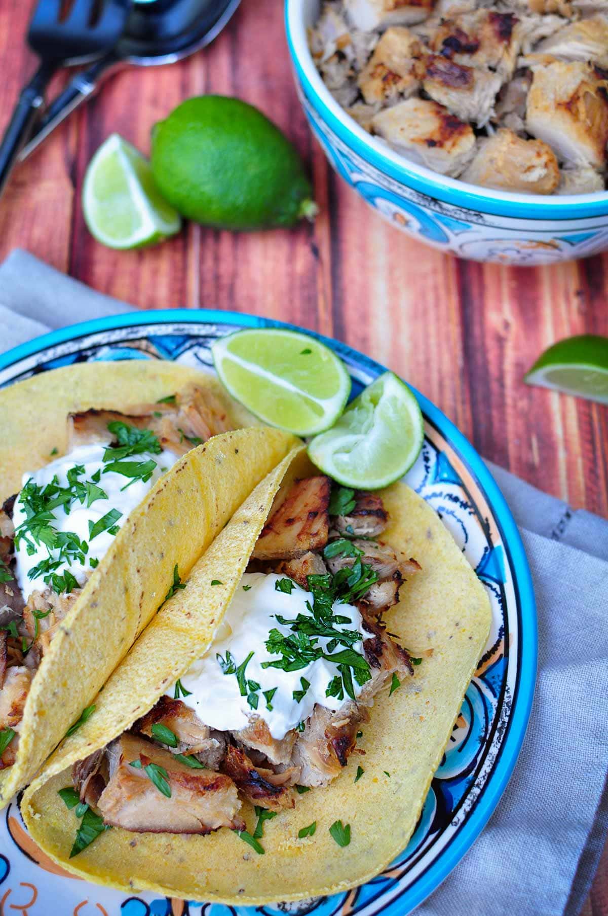 Carnitas tacos on table alongside bowl of Slow Cooker Carnitas.