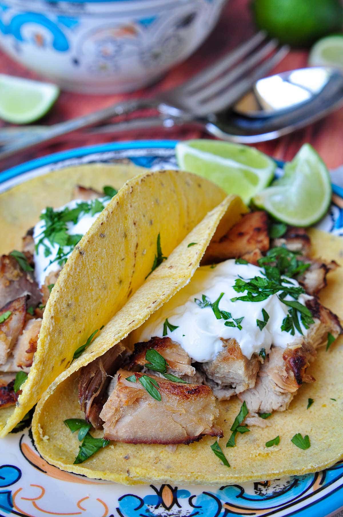 Carnitas tacos on blue plate with lime wedges in background.