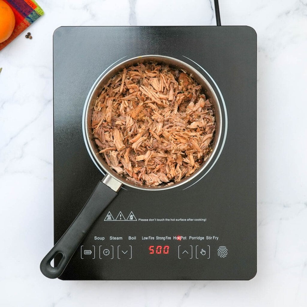 How to make carnitas by combining shredded pork with cooking liquids in pot.